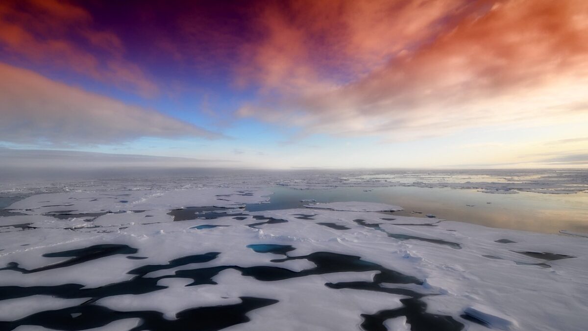 Banquise plane sous un ciel de coucher de soleil aux nuages rouges et violets, avec des flaques de fonte sombres et une étendue d'eau au loin.
