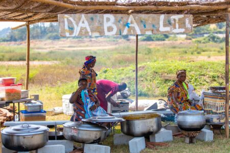 African women cooking in pots at a market stall, showcasing traditional culinary practices.