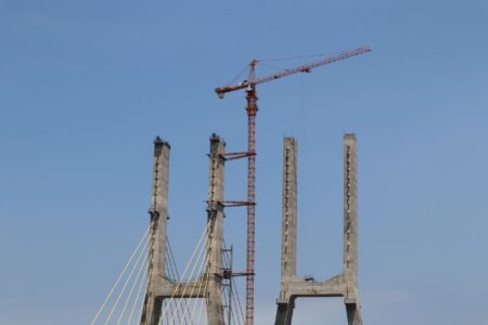 Construction of a tall cable-stayed bridge with a crane under a clear blue sky.
